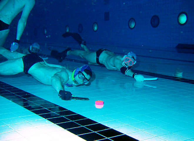 Deux joueurs de hockey subaquatique au fond de la piscine chassant le palet.
